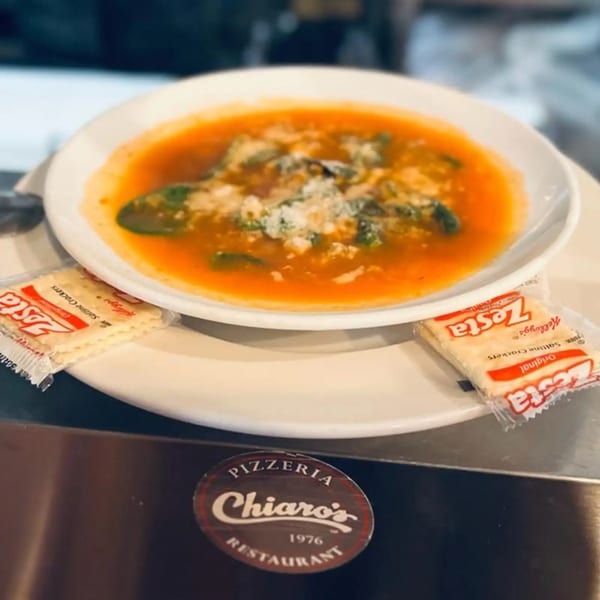 A bowl of Chiaro's Pizzeria & Restaurant's tomato soup with spinach and cheese, served with crackers.