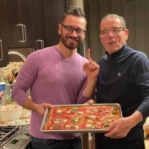 Two men proudly holding a rectangular Chiaro's Pizzeria pizza with basil and cheese.