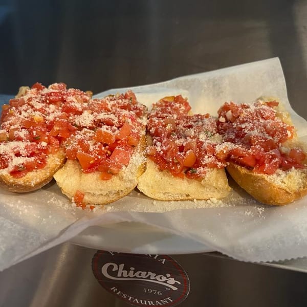 Four bruschetta pieces topped with diced tomatoes and grated cheese on white paper, with a Chiaro's logo visible.