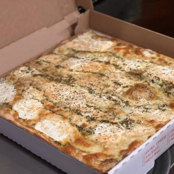 A square white pizza with dollops of ricotta cheese and herbs in a cardboard box.