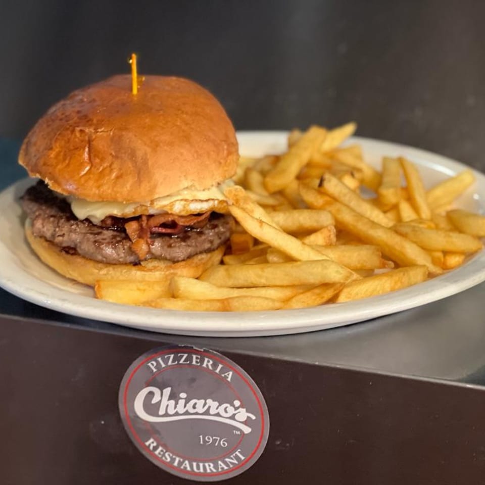 A Chiaro's burger with cheese, bacon, and a fried egg, served with a side of fries.