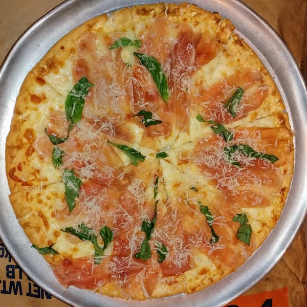 A Chiaro's Pizzeria pizza with prosciutto, basil, and grated cheese on a metal pan.