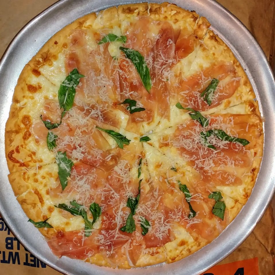 A Chiaro's Pizzeria pizza with prosciutto, basil, and grated cheese on a metal pan.