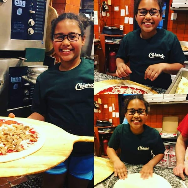 A smiling girl in a Chiaro's Pizzeria shirt making and holding pizzas with various toppings.