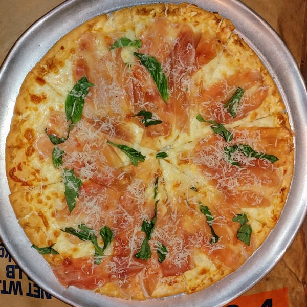 A whole Chiaro's Pizzeria & Restaurant pizza with prosciutto, basil, and shredded cheese.