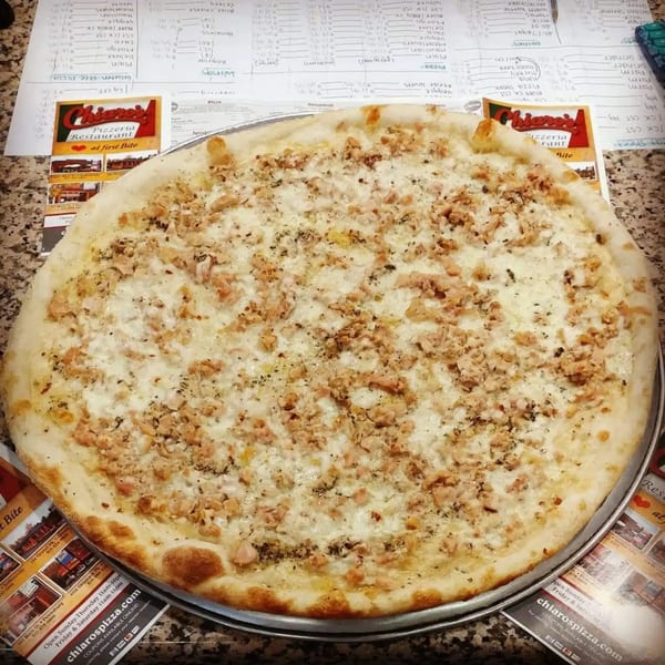 A Chiaro's Pizzeria white pizza with chicken, cheese, and herbs on a metal pan.