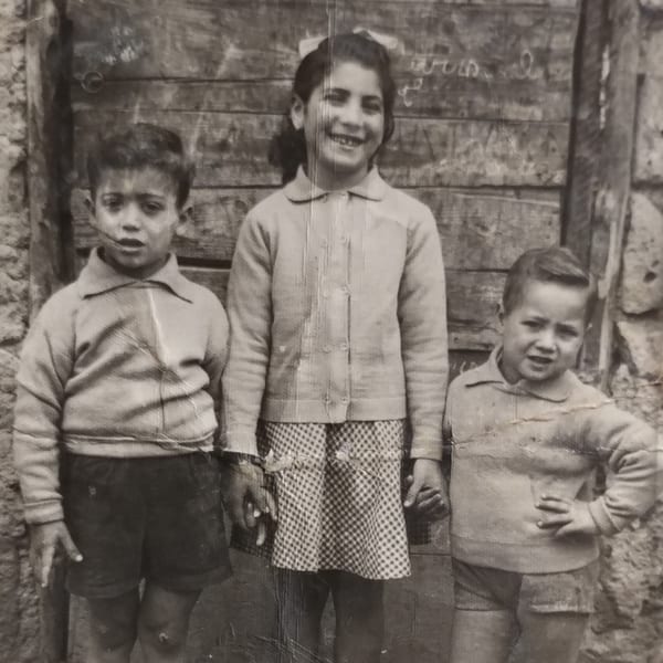 Black and white photo of three young children, two boys and a girl, standing together.