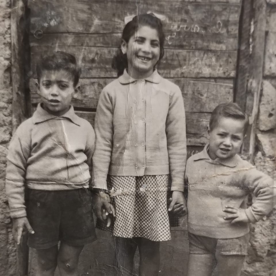 Black and white photo of three young children, two boys and a girl, standing together.