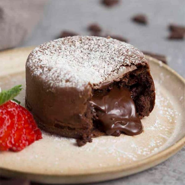 Molten chocolate lava cake with powdered sugar, a strawberry, and mint on a plate.