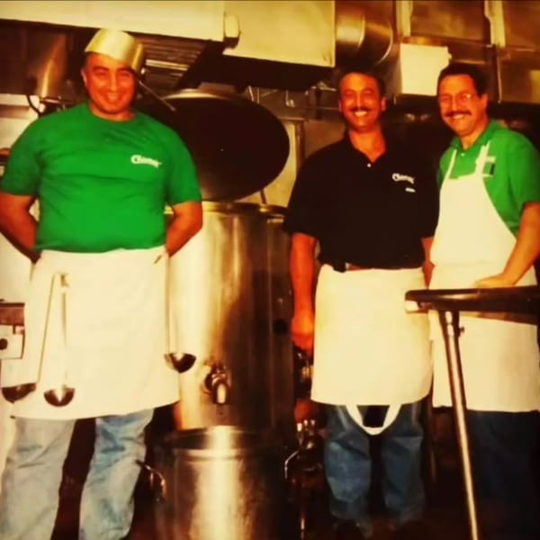Three smiling men in aprons and Chiaro's shirts stand in a commercial kitchen.