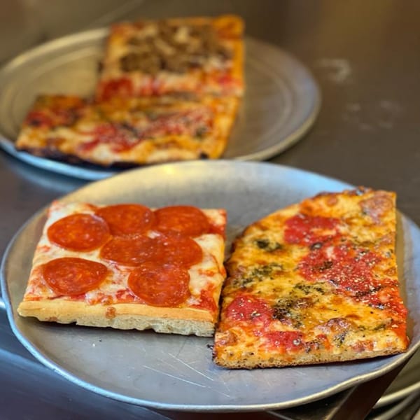 Two metal trays with various slices of Chiaro's Pizzeria pizza, including pepperoni and plain.
